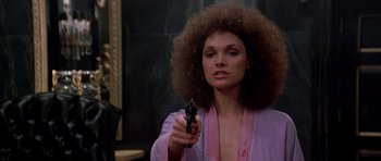 Movie still from “Scarface” (1983), directed by Brian De Palma – A woman holding a gun while standing in front of a mirror; Close Up shot, Over the shoulder angle