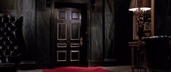 Movie still from “Scarface” (1983), directed by Brian De Palma – A black door in a room with a red rug; Wide shot, High angle