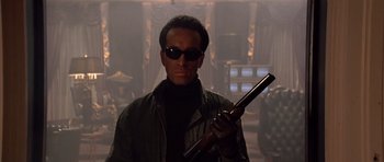 Movie still from “Scarface” (1983), directed by Brian De Palma – A man with sunglasses holding a gun in a room; Medium shot, Low angle