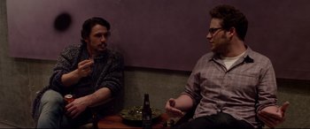 Movie still from “This Is the End” (2013), directed by Seth Rogen – Two men sitting at a table with a bottle of beer; Medium shot, Over the shoulder angle