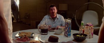 Movie still from “This Is the End” (2013), directed by Seth Rogen – A man sitting at a table with a plate of cake; Medium shot, Over the shoulder angle