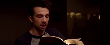 Movie still from “This Is the End” (2013), directed by Seth Rogen – A man reading a book in a dark room; Close Up shot, Over the shoulder angle