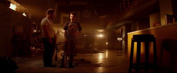 Movie still from “This Is the End” (2013), directed by Seth Rogen – A man standing next to another man in a dark room; Wide shot, Low angle
