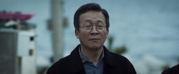 Movie still from “Time to Hunt” (2020), directed by Yoon Sunghyun – An older man with glasses and a black jacket; Close Up shot, Over the shoulder angle