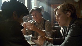 Movie still from “Titanic” (1997), directed by James Cameron – A group of people sitting at a table with drinks; Medium shot, Over the shoulder angle