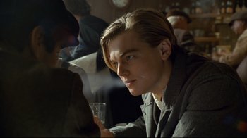 Movie still from “Titanic” (1997), directed by James Cameron – A man sitting at a table holding a glass of wine; Close Up shot, Over the shoulder angle