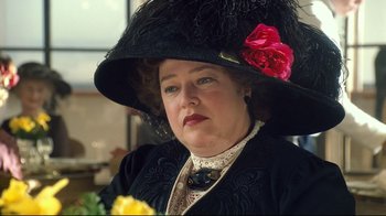 Movie still from “Titanic” (1997), directed by James Cameron – An older woman wearing a large black hat and holding a yellow rose; Close Up shot, Over the shoulder angle