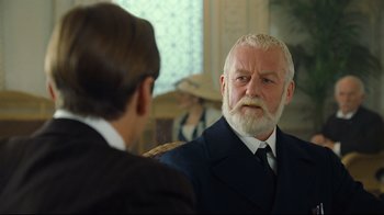 Movie still from “Titanic” (1997), directed by James Cameron – A man in a suit and a white beard is talking to another man in a suit; Close Up shot, Over the shoulder angle