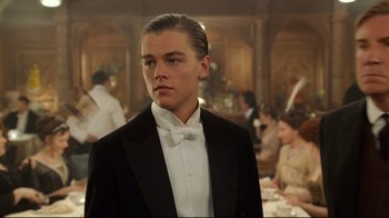 Movie still from “Titanic” (1997), directed by James Cameron – A man in a tuxedo standing in front of a table; Medium shot, Low angle