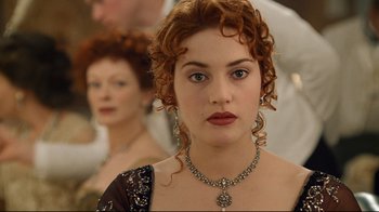 Movie still from “Titanic” (1997), directed by James Cameron – A person with curly hair wearing a necklace; Close Up shot, Over the shoulder angle
