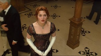 Movie still from “Titanic” (1997), directed by James Cameron – A woman with red hair wearing white gloves and a black dress; Medium shot, High angle