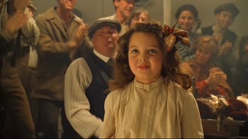 Movie still from “Titanic” (1997), directed by James Cameron – A little girl with a bow in her hair standing in front of a group of people; Close Up shot, Over the shoulder angle