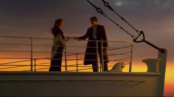 Movie still from “Titanic” (1997), directed by James Cameron – A man and a woman standing next to a railing on a boat; Wide shot, Low angle