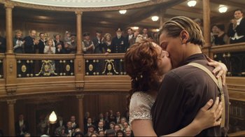 Movie still from “Titanic” (1997), directed by James Cameron – A couple kissing in front of a crowd of people in a theater; Medium shot, Low angle