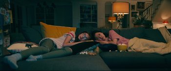 Movie still from “To All the Boys I've Loved Before” (2018), directed by Susan Johnson – Two young girls laying on a couch watching tv; Medium shot, High angle