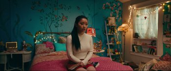 Movie still from “To All the Boys I've Loved Before” (2018), directed by Susan Johnson – A woman sitting on top of a bed in a room; Medium shot, High angle