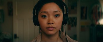 Movie still from “To All the Boys I've Loved Before” (2018), directed by Susan Johnson – A woman wearing headphones and looking at the camera; Close Up shot, High angle