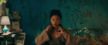 Movie still from “To All the Boys I've Loved Before” (2018), directed by Susan Johnson – A woman holding a pair of headphones in her hands; Medium shot, Over the shoulder angle