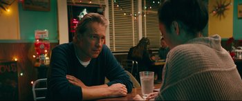 Movie still from “To All the Boys I've Loved Before” (2018), directed by Susan Johnson – A man sitting at a table in front of a glass of water; Medium shot, Over the shoulder angle