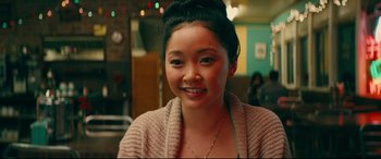 Movie still from “To All the Boys I've Loved Before” (2018), directed by Susan Johnson – A young woman smiles for the camera in a restaurant; Close Up shot, Over the shoulder angle