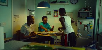 Movie still from “Top Boy” (2011), created by Ronan Bennett – A group of men sitting at a table in a room; Medium shot, Low angle