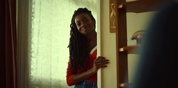 Movie still from “Top Boy” (2011), created by Ronan Bennett – A woman with dreadlocks leaning against a wall; Medium shot, Over the shoulder angle