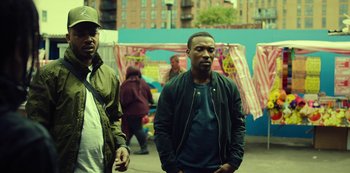 Movie still from “Top Boy” (2011), created by Ronan Bennett – A man in a green jacket standing next to another man in a green jacket; Medium shot, Over the shoulder angle