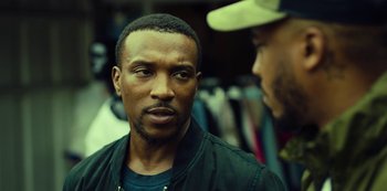 Movie still from “Top Boy” (2011), created by Ronan Bennett – A man in a black jacket and a man in a white hat; Close Up shot, Over the shoulder angle