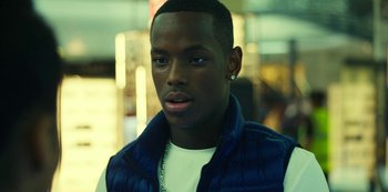 Movie still from “Top Boy” (2011), created by Ronan Bennett – A young man with a white t - shirt and a blue vest; Close Up shot, Over the shoulder angle