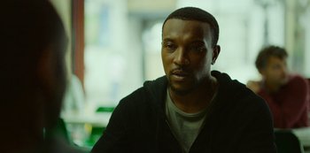 Movie still from “Top Boy” (2011), created by Ronan Bennett – A person sitting in a room; Close Up shot, Low angle