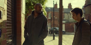 Movie still from “Top Boy” (2011), created by Ronan Bennett – A man standing on the side of the street; Medium shot, Low angle