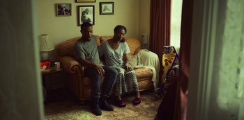 Movie still from “Top Boy” (2011), created by Ronan Bennett – A man and a woman sitting on a couch in a living room; Wide shot, High angle