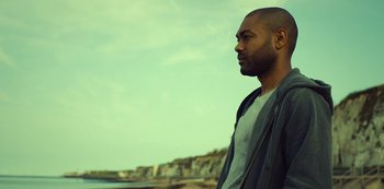 Movie still from “Top Boy” (2011), created by Ronan Bennett – A person standing near a body of water; Medium shot, Low angle