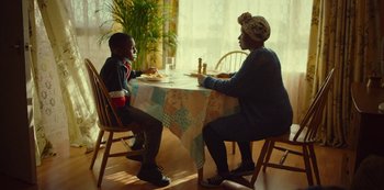 Movie still from “Top Boy” (2011), created by Ronan Bennett – Two people sitting at a table with a plate of food; Medium shot, Over the shoulder angle