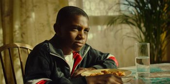 Movie still from “Top Boy” (2011), created by Ronan Bennett – A young man sitting at a table with a slice of pizza; Close Up shot, Low angle