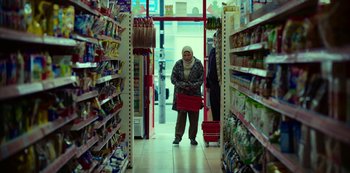 Movie still from “Top Boy” (2011), created by Ronan Bennett – A woman is standing in a grocery store with a shopping cart; Wide shot, Low angle