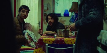 Movie still from “Top Boy” (2011), created by Ronan Bennett – A group of people sitting around a dinner table; Medium shot, Over the shoulder angle