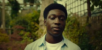 Movie still from “Top Boy” (2011), created by Ronan Bennett – A young man with a beard is standing in front of a tree; Close Up shot, Low angle