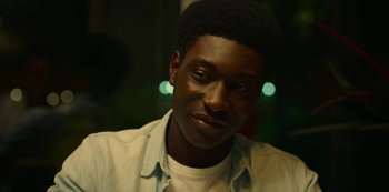 Movie still from “Top Boy” (2011), created by Ronan Bennett – A person smiling for the camera; Close Up shot, Over the shoulder angle