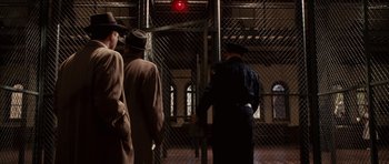 Movie still from “Shutter Island” (2010), directed by Martin Scorsese – A group of men standing next to each other in front of a chain link fence; Wide shot, Low angle