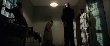 Movie still from “Shutter Island” (2010), directed by Martin Scorsese – Two men in suits and hats standing in a dimly - lit room; Wide shot, Low angle