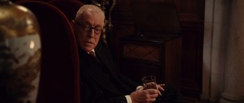 Movie still from “Shutter Island” (2010), directed by Martin Scorsese – An older man sitting in a chair holding a glass of wine; Medium shot, Low angle