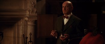 Movie still from “Shutter Island” (2010), directed by Martin Scorsese – A man in a suit and bow tie holding a cigarette; Medium shot, Low angle