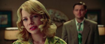 Movie still from “Shutter Island” (2010), directed by Martin Scorsese – A woman with blonde hair is smiling at the camera while a man stands in the background; Close Up shot, Over the shoulder angle