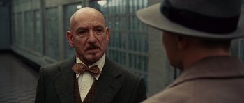 Movie still from “Shutter Island” (2010), directed by Martin Scorsese – An older bald man wearing a suit and bow tie; Close Up shot, Over the shoulder angle