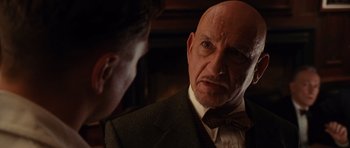 Movie still from “Shutter Island” (2010), directed by Martin Scorsese – An older man wearing a suit and bow tie; Close Up shot, Over the shoulder angle