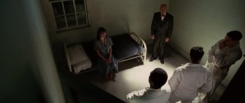 Movie still from “Shutter Island” (2010), directed by Martin Scorsese – Two men and a woman standing in front of a bed in a room; Wide shot, High angle