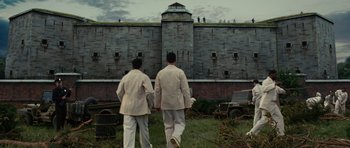 Movie still from “Shutter Island” (2010), directed by Martin Scorsese – A couple of men walking next to each other near a building; Extreme Wide shot, Low angle