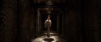 Movie still from “Shutter Island” (2010), directed by Martin Scorsese – A man standing in a dark hallway with lights on; Wide shot, High angle