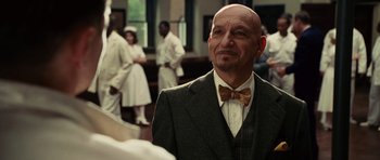 Movie still from “Shutter Island” (2010), directed by Martin Scorsese – A bald man in a suit and bow tie; Close Up shot, Over the shoulder angle